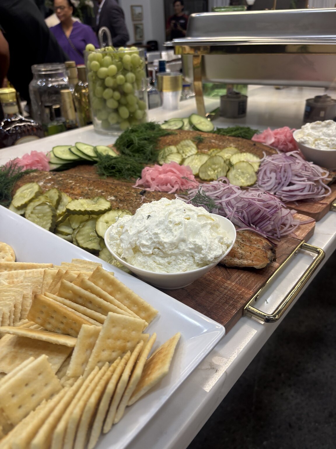 A smoked salmon grazing display with crackers, pickles, onions, and herbed spread